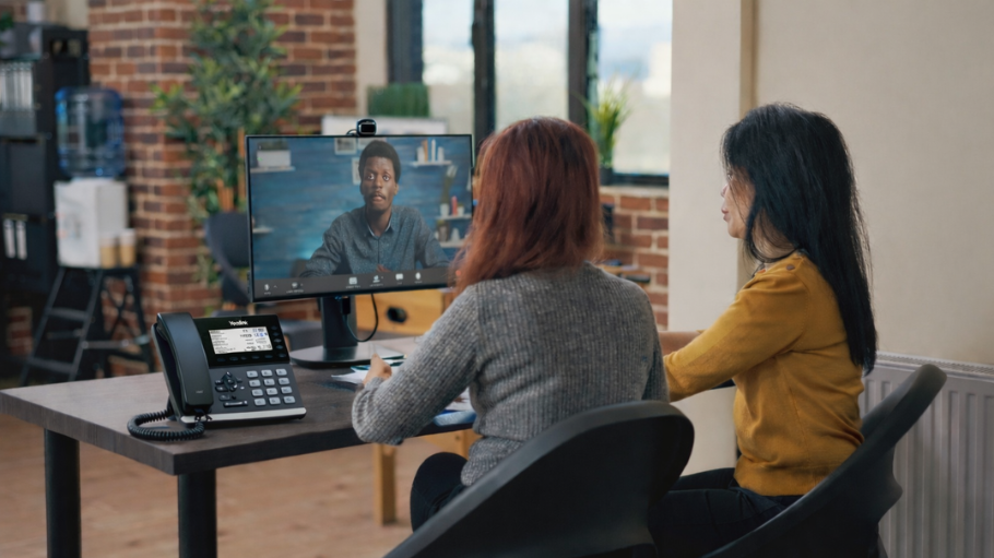 Modern office workspace showing integrated voip and internet setup; two professionals at a desk during a video call.