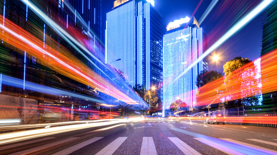 Abstract long-exposure light trails representing high-speed data flow and modern telecom terms and acronyms in a vibrant city skyline at night.
